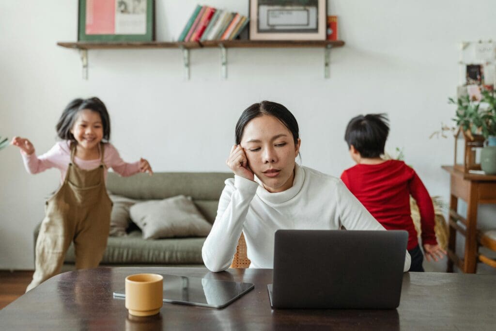pexels photo 4474035 4474035 A tired mother working on a laptop while her children play around indoors, highlighting remote work challenges.